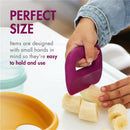 Toddler using a purple food prep tool to slice bananas, showcasing the Boon INTRO set designed for easy handling.