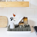 Countertop drying rack with gray/white design holding two amber glasses and a white cup, featuring drying straw-like spikes.
