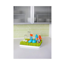 Countertop drying rack with green grass-like base, featuring colorful utensils and glassware.