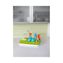Countertop drying rack with green grass-like base, featuring colorful utensils and glassware.