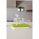 Boon TWIG drying rack accessory in white with a green grass-like base, holding baby bottles and lids for drying.