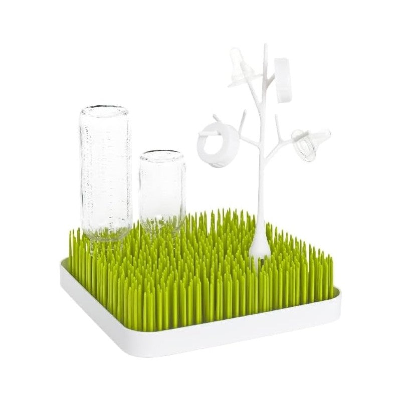 Boon TWIG Drying Rack Accessory in white with green grass-like base, holding baby bottles and pacifiers for drying.