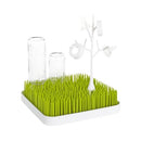 Boon TWIG Drying Rack Accessory in white with green grass-like base, holding baby bottles and pacifiers for drying.