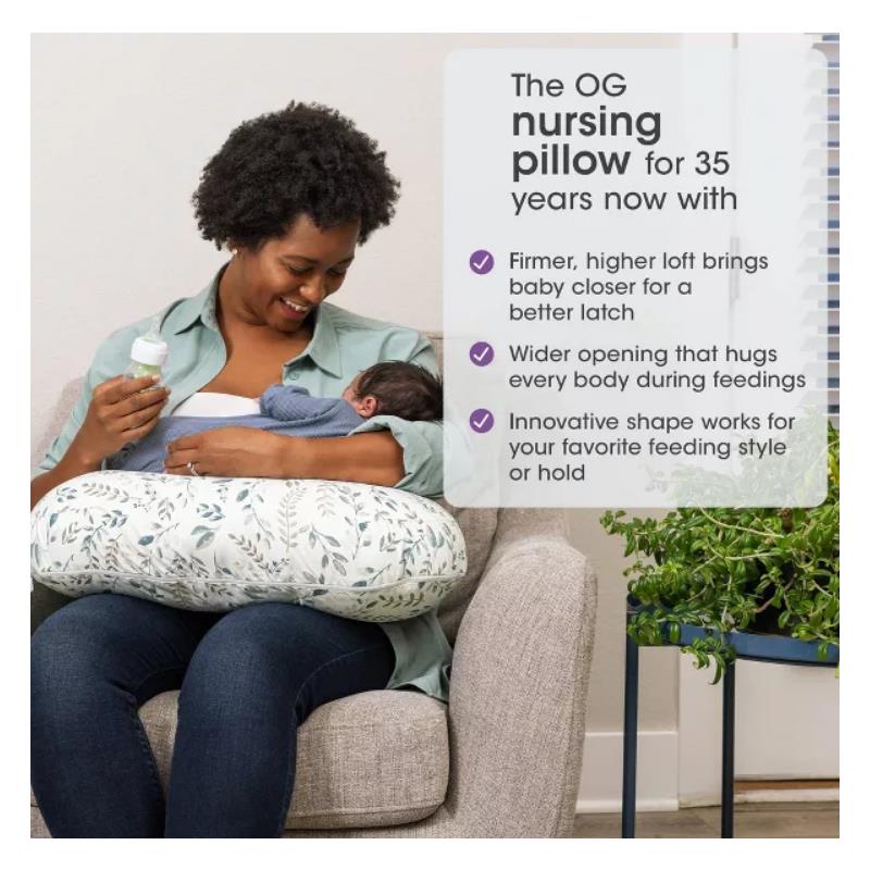 Boppy Nursing Pillow in beige foliage design, supporting a woman feeding a baby with a bottle.
