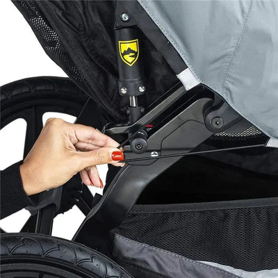 A hand adjusts the locking mechanism of a Britax Gear Duallie Swivel Wheel Stroller Weather Shield, showcasing its features.