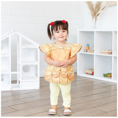 Bumkins Disney Princess Ruffle Apron Bib in Belle design worn by a young girl, featuring golden fabric and ruffled sleeves.