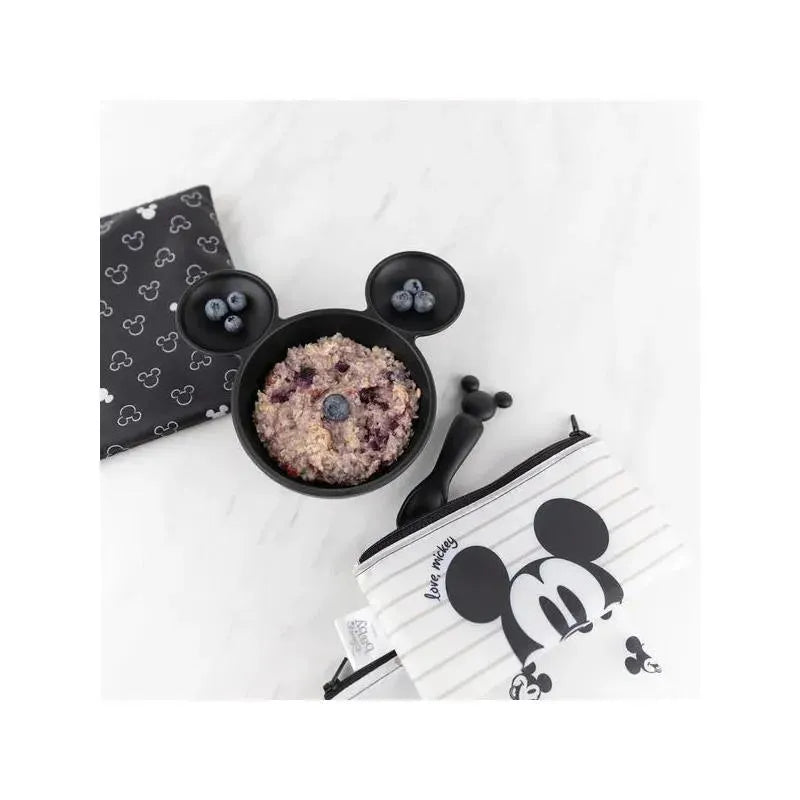 Black silicone bowl with mouse ears holding oatmeal and blueberries, accompanied by a patterned cloth and a zippered pouch.