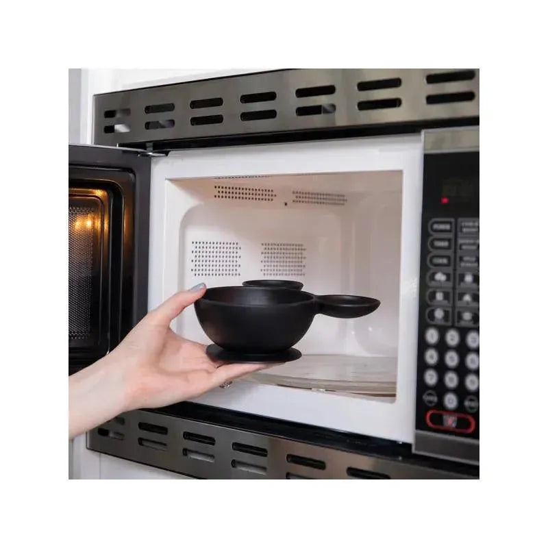 Bumkins Disney silicone feeding bowl being placed inside a microwave by a hand, showcasing its black color and handle.