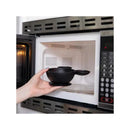Bumkins Disney silicone feeding bowl being placed inside a microwave by a hand, showcasing its black color and handle.