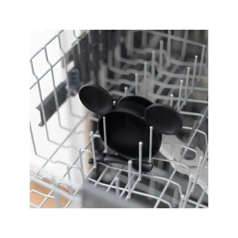 Black silicone feeding set shaped like Mickey Mouse, resting in a dishwasher rack, ready for cleaning.