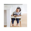 Toddler seated in a high chair wearing a Mickey Mouse bib, with a brown silicone feeding set on the tray.
