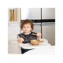 Toddler wearing a Disney-themed bib, sitting in a high chair with a gold feeding bowl filled with food.