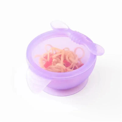 Silicone feeding set in purple with a suction base, featuring a bowl and a spoon, filled with noodles and small pieces.