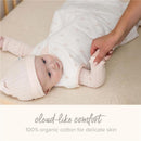 Baby in a soft, light-colored sleeping bag, with a caregiver gently holding their arm; features the text “cloud-like comfort 100% organic cotton for delicate skin.”