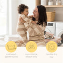 A mother and her baby, both in matching beige-striped outfits, smile and play together in a bright laundry room, surrounded by neatly folded towels. Care instructions for laundry are displayed below.