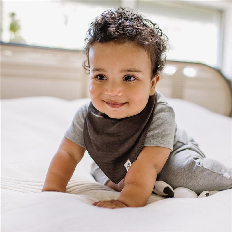 Smiling baby wearing a brown bandana bib, crawling on a light-colored blanket.