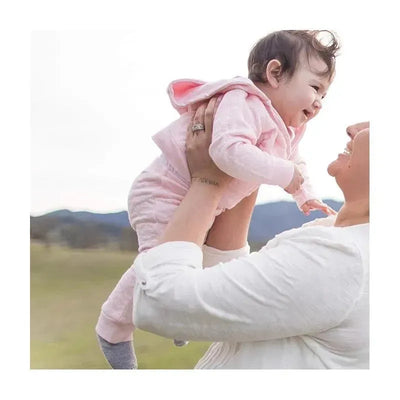 Baby girl wearing pink knit jogger pants with a hood, lifted happily by a woman outdoors.