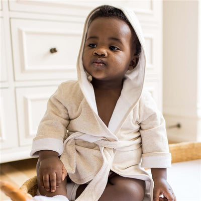 Hooded oatmeal robe on an infant, sitting with a neutral expression, showcasing a soft and cozy garment design.