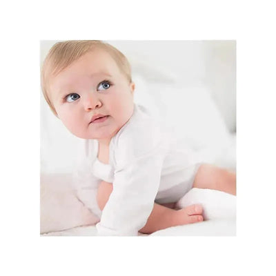 A baby in a white long sleeve bodysuit sits on a soft surface, looking curiously to the side.