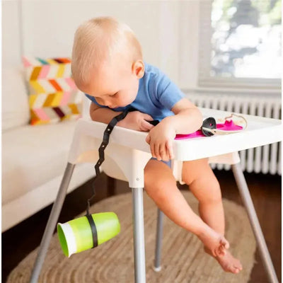 Toddler in a high chair using the Busy Baby Bottle Bungee to secure a green cup.