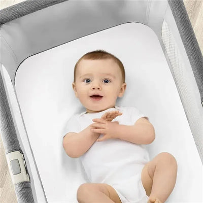 Chicco Lullago Bassinet Sheets in white with a smiling baby wearing a white onesie lying inside the bassinet.