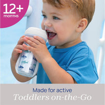 Chicco Insulated Rim Spout Trainer Sippy Cup in blue with shark designs, held by a toddler smiling while drinking.