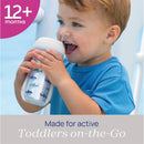 Chicco Insulated Rim Spout Trainer Sippy Cup in blue with shark designs, held by a toddler smiling while drinking.