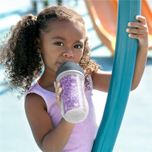Toddler with curly hair holds a Chicco insulated straw sippy cup, decorated with a floral purple print, at a playground.