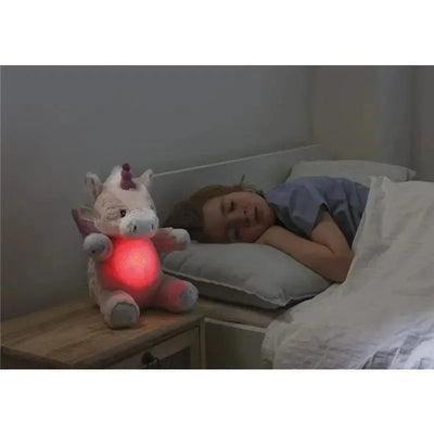 Soft plush unicorn nightlight with a glowing red heart beside a sleeping child in bed.