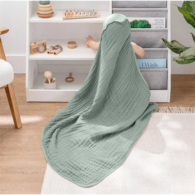Hooded towel in fern color draped over a child sitting on the floor, surrounded by toys and a shelf of books.