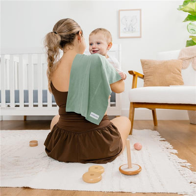 Mom holding a smiling baby, using a green burp cloth, in a warmly decorated nursery with toys and a crib.