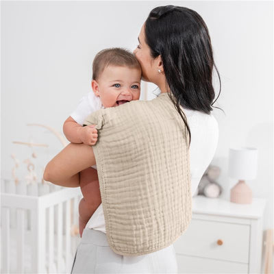 Muslin burp cloth in sand color draped over a caregiver’s shoulder, with a smiling baby being held.
