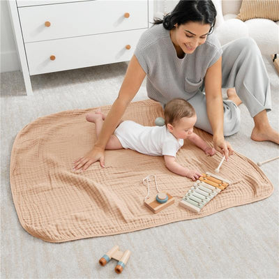 Muslin baby blanket in cream, with a mother and baby playing with wooden toys on it, creating a cozy playtime setting.