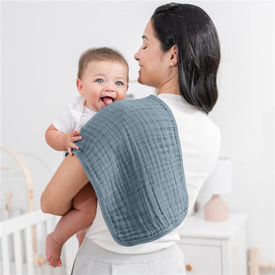 Muslin burp cloth draped over a woman’s shoulder, holding a smiling baby; soft, textured fabric in a muted blue.