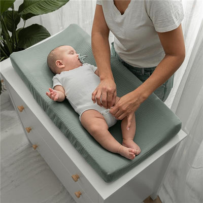 Muslin fitted changing pad cover in fern color with a baby in a onesie, being attended to by a caregiver.