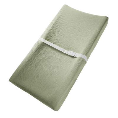 Muslin fitted changing pad cover in sage green, featuring a textured surface and a white strap for secure fitting.