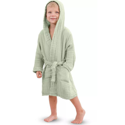 A smiling child wearing a sage-colored muslin bathrobe with a hood, showing a cozy and playful look.
