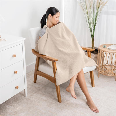Muslin nursing cover in sand color, draped over a woman seated in a chair, providing privacy while nursing.