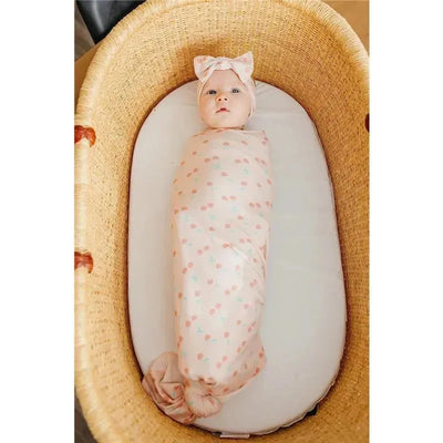 Baby swaddled in a patterned Copper Pearl blanket, laying in a wicker bassinet, wearing a matching headband.