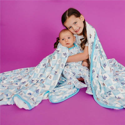 A girl and a baby wrapped in a colorful Copper Pearl Monsters Inc themed quilt, smiling against a purple background.