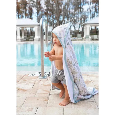 Toddler in a hooded copper pearl bath towel with floral pattern, standing by a pool, gripping a railing.