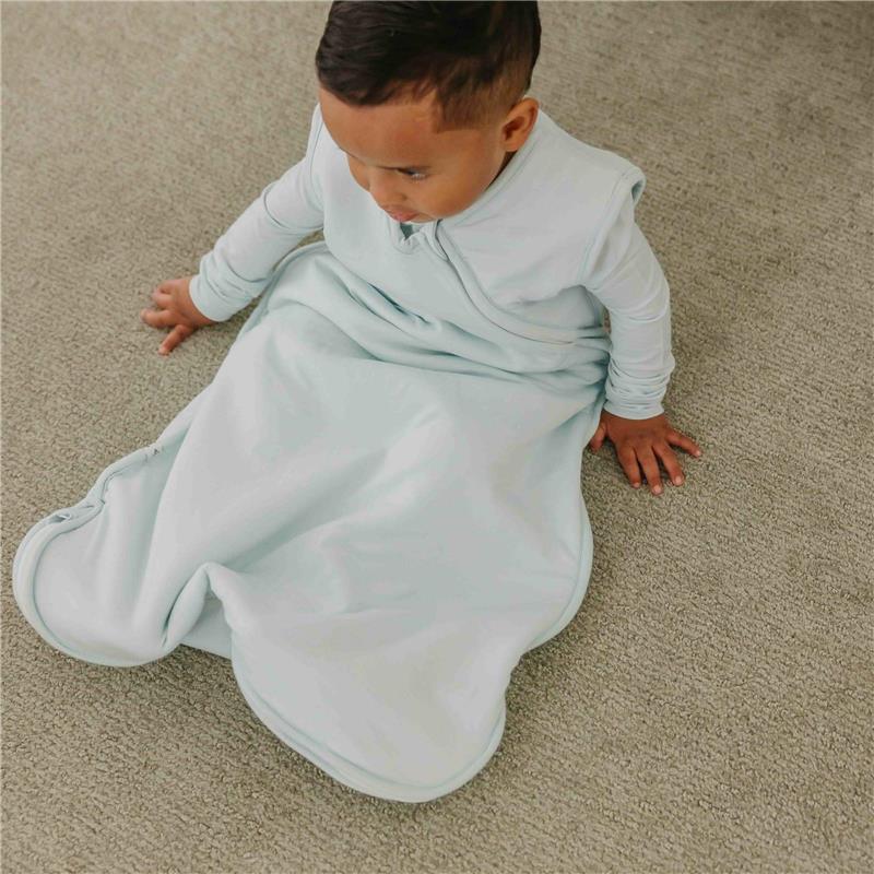 Light blue 0.5 Tog sleep bag designed for infants, worn by a baby sitting on a carpeted floor.