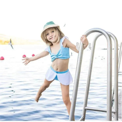 Young child playing on a swimming pool ladder, wearing a blue and white Cinderella-themed two-piece swimsuit.