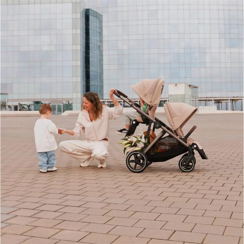 Cybex Gazelle S Second Seat in taupe and chocolate brown, with a woman interacting with a child beside the stroller.