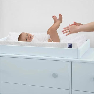 Contoured changing pad with a grey stripe fabric, featuring a baby smiling and kicking, with a hand reaching towards them.