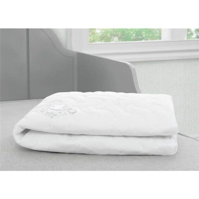 White Delta Sertapedic fitted crib mattress pad folded neatly on a gray surface, showcasing a quilted texture.