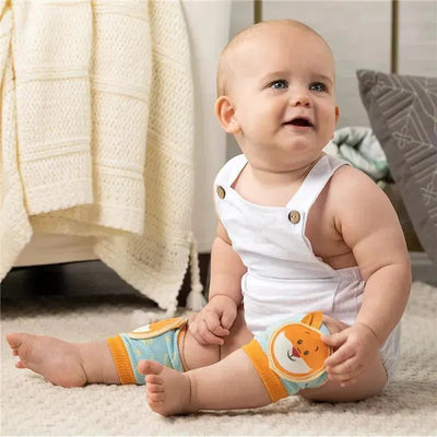 Baby sitting on a soft rug, wearing a white outfit and colorful fox-themed knee pads, looking joyful and playful.