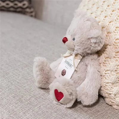 Plush bear with a red nose and a heart on its paw, labeled as January birthstone, garnet.