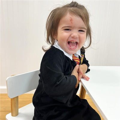 Toddler wearing a Harry Potter costume with a Gryffindor tie, smiling while seated at a table.