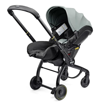 Doona X Infant Car Seat in Dusty Sage color with a black base, featuring a sunshade and safety labels.